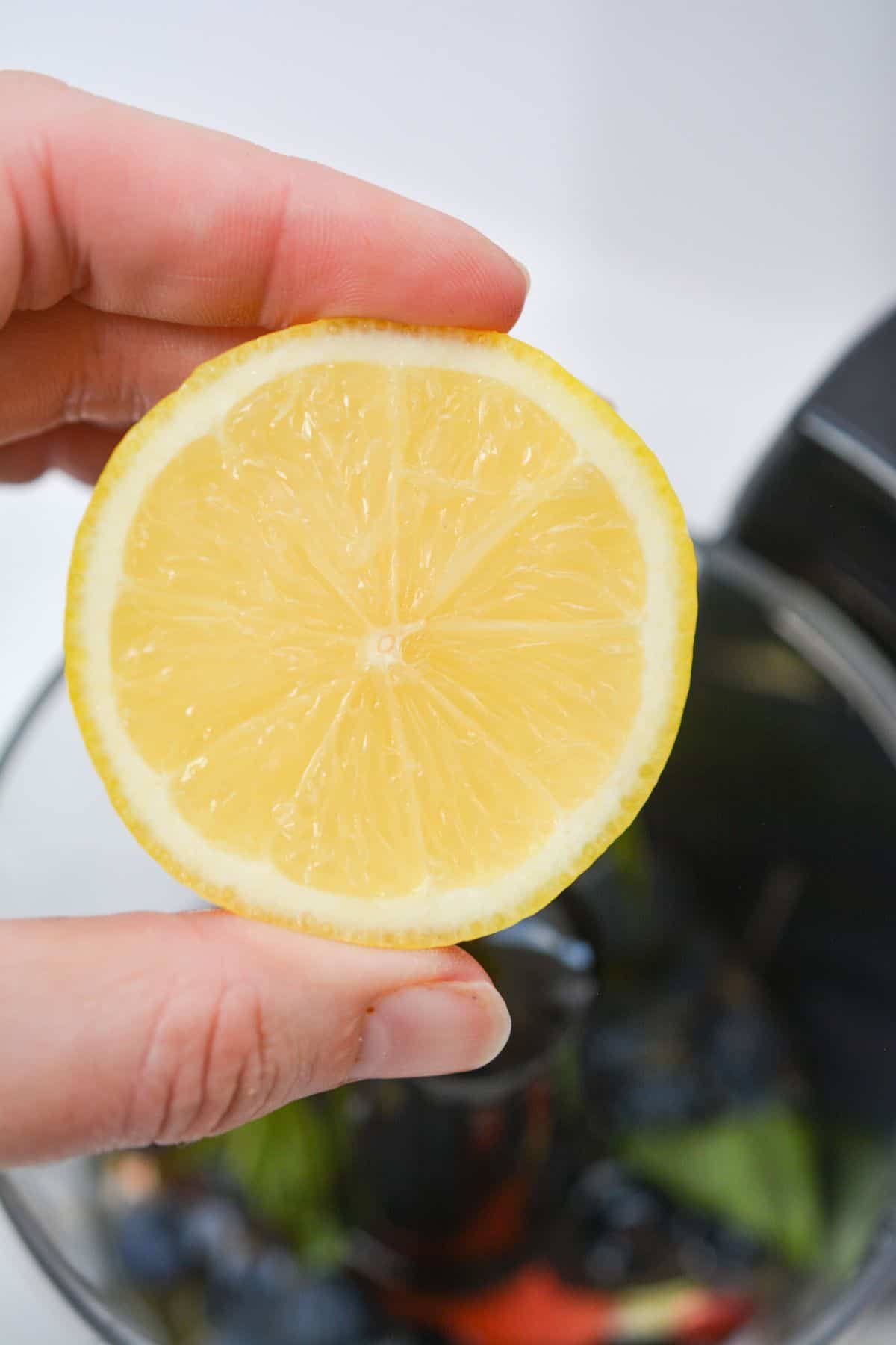 A person holding a slice of lemon in a food processor.
