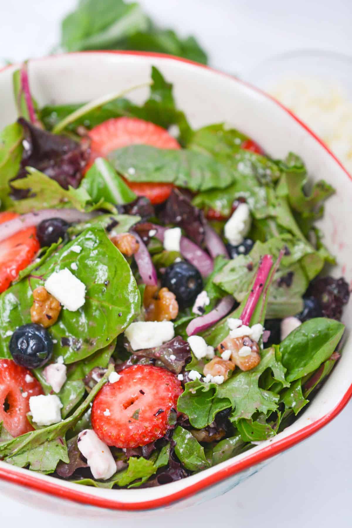 A bowl of salad with strawberries, blueberries and feta cheese.