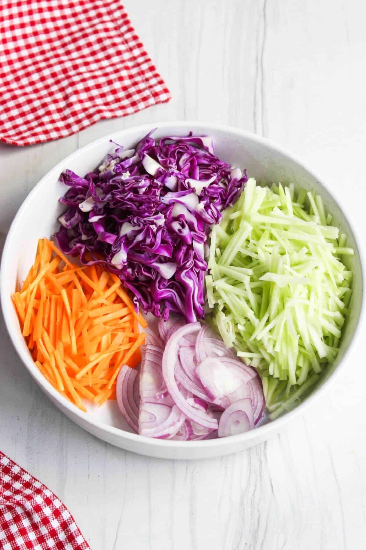 Shredded cabbage and carrots with sliced red onion and red cabbage in a bowl.