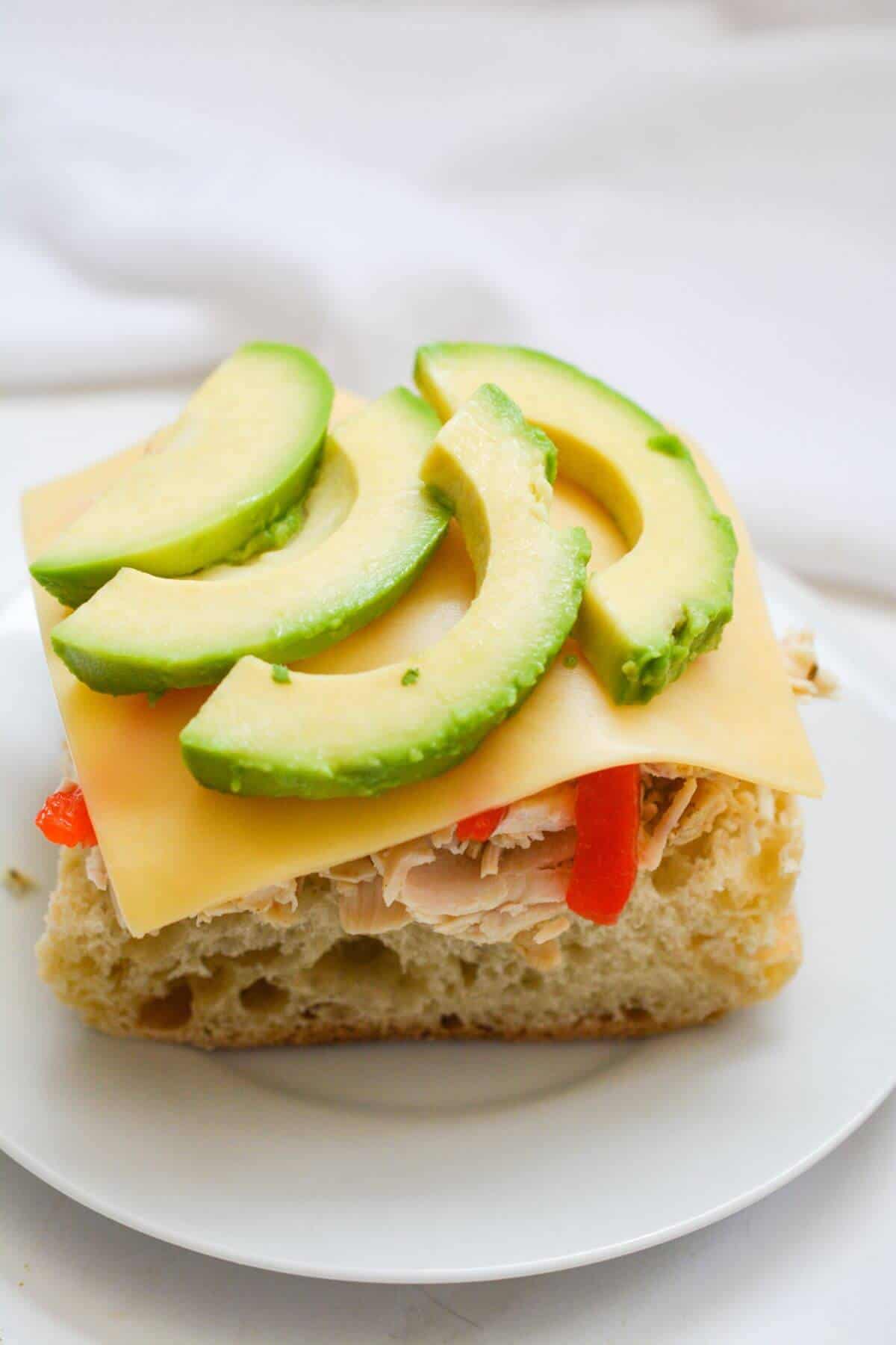 Slice of gouda cheese and sliced avocado added to sandwich.