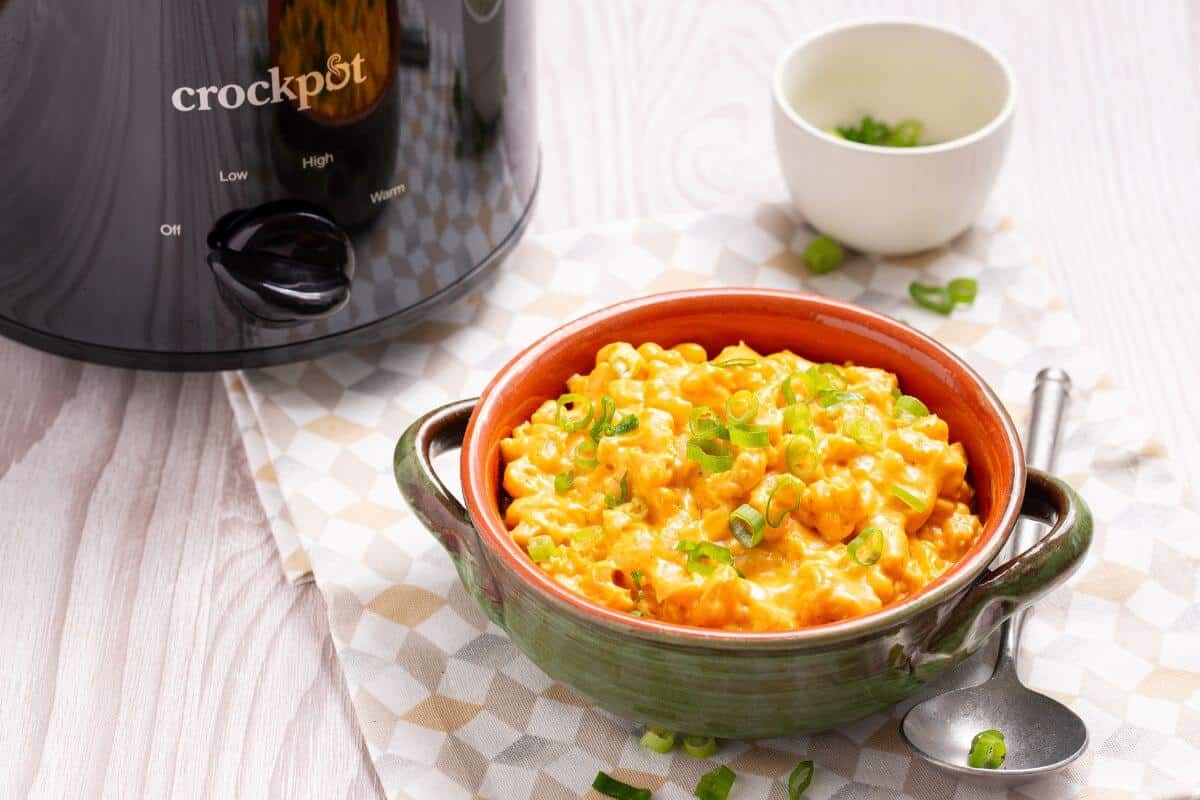 A bowl of macaroni and cheese in front of a slow cooker.