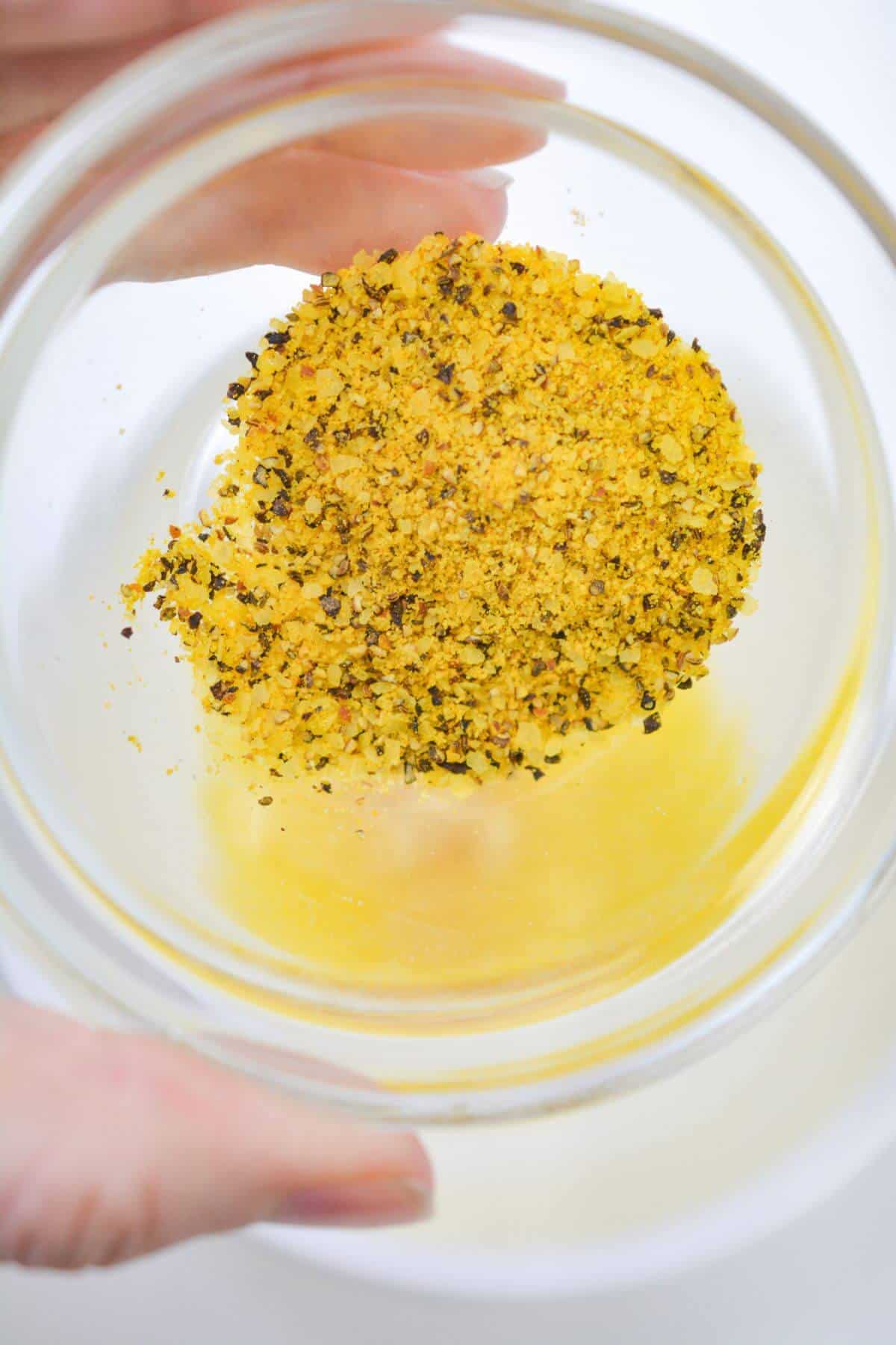 Adding lemon pepper seasoning to melted butter in bowl.