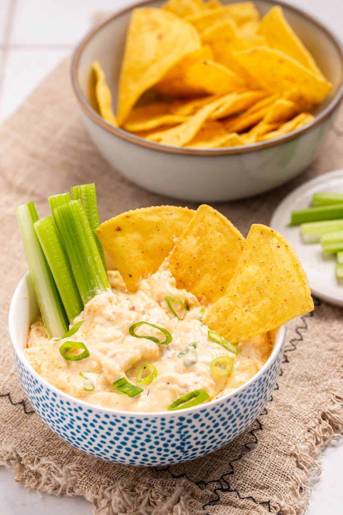 Serving buffalo chicken dip in bowl with chips and celery sticks.