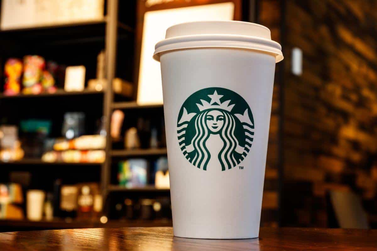 A Starbucks cup, featuring a hot drink, sits on a wooden table.