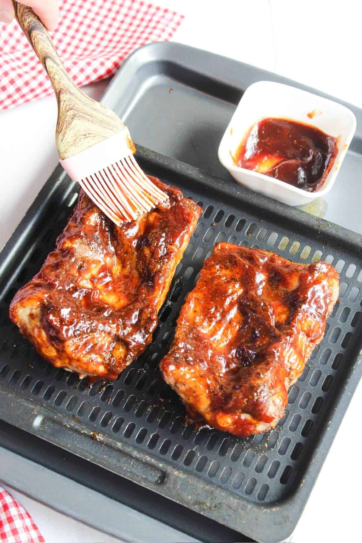 BBQ pork ribs on an air fryer tray with a brush.