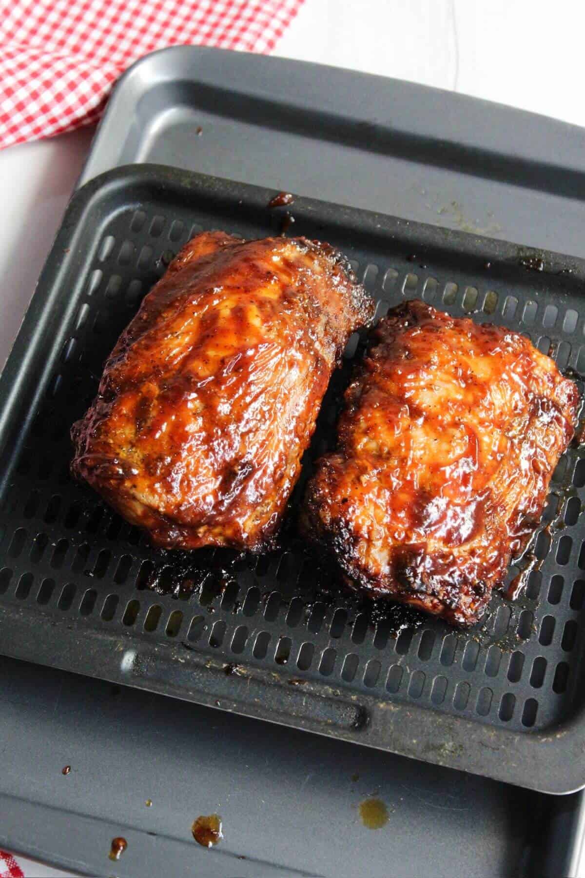 Two pieces of BBQ pork ribs on an air fryer tray.