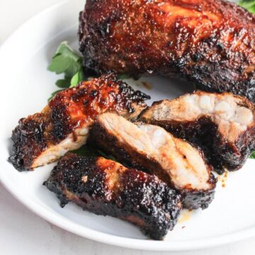 BBQ ribs on a white plate with greens.