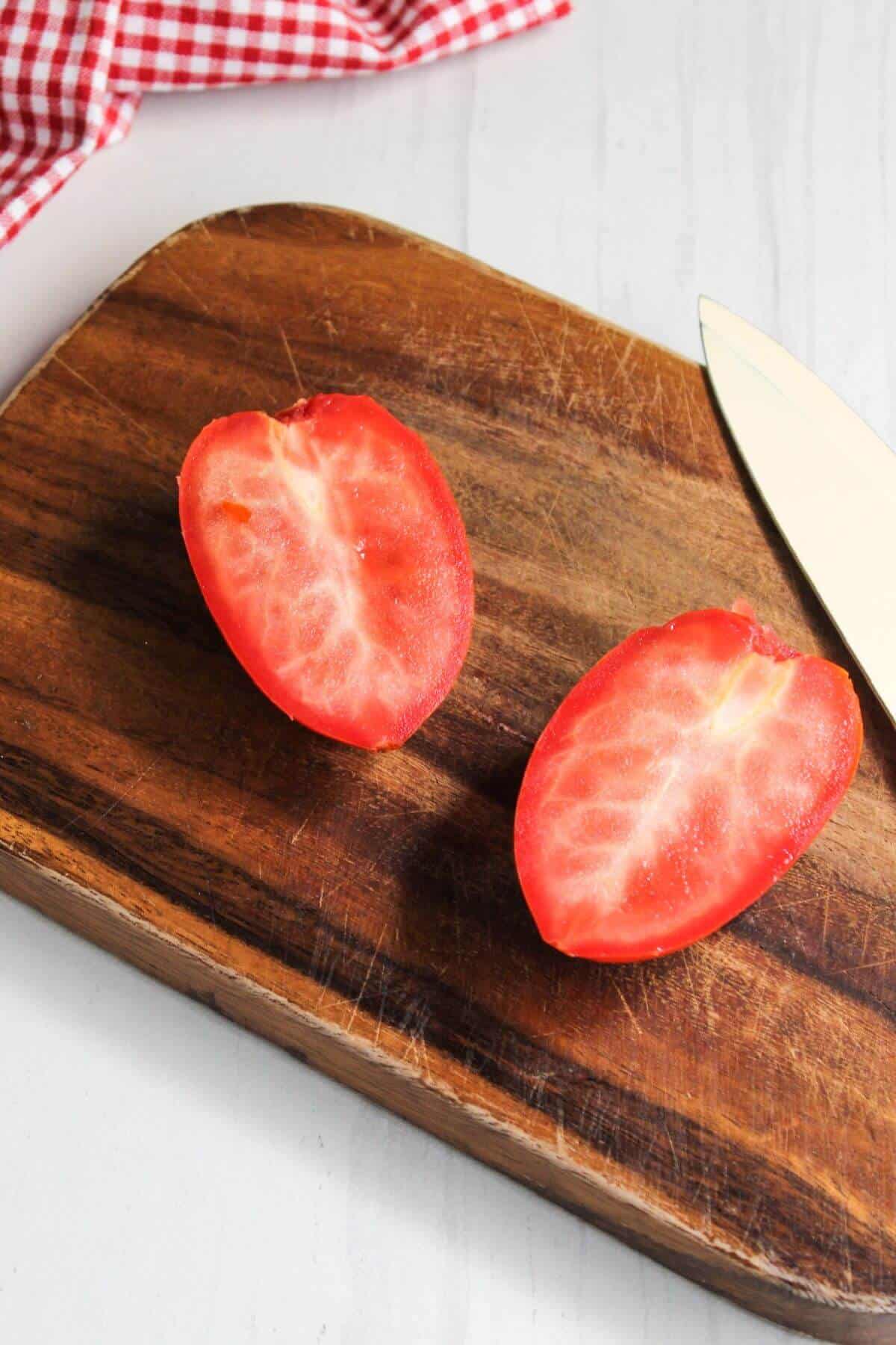 Two tomatoes on a cutting board with a knife.