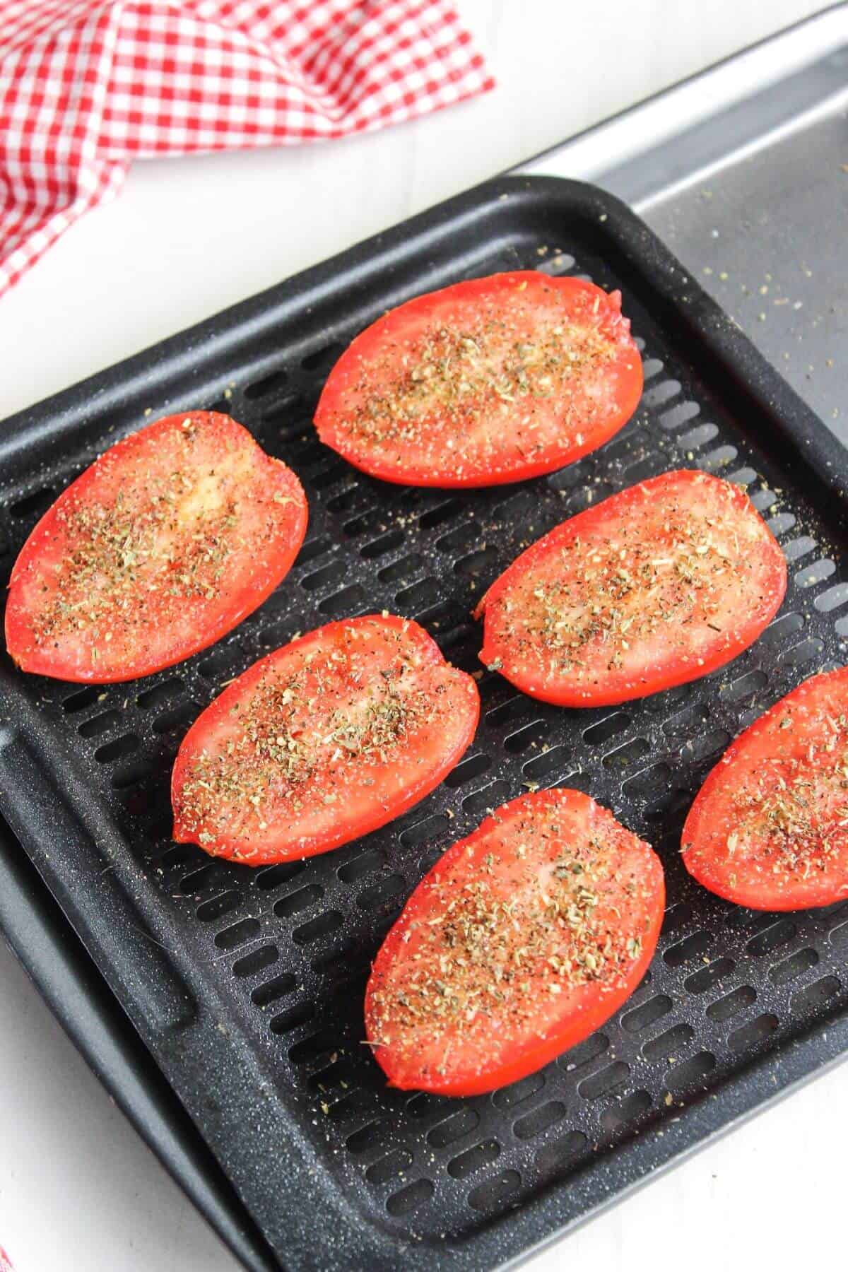 Tomatoes on an air fryer tray with a checkered checkered tablecloth.