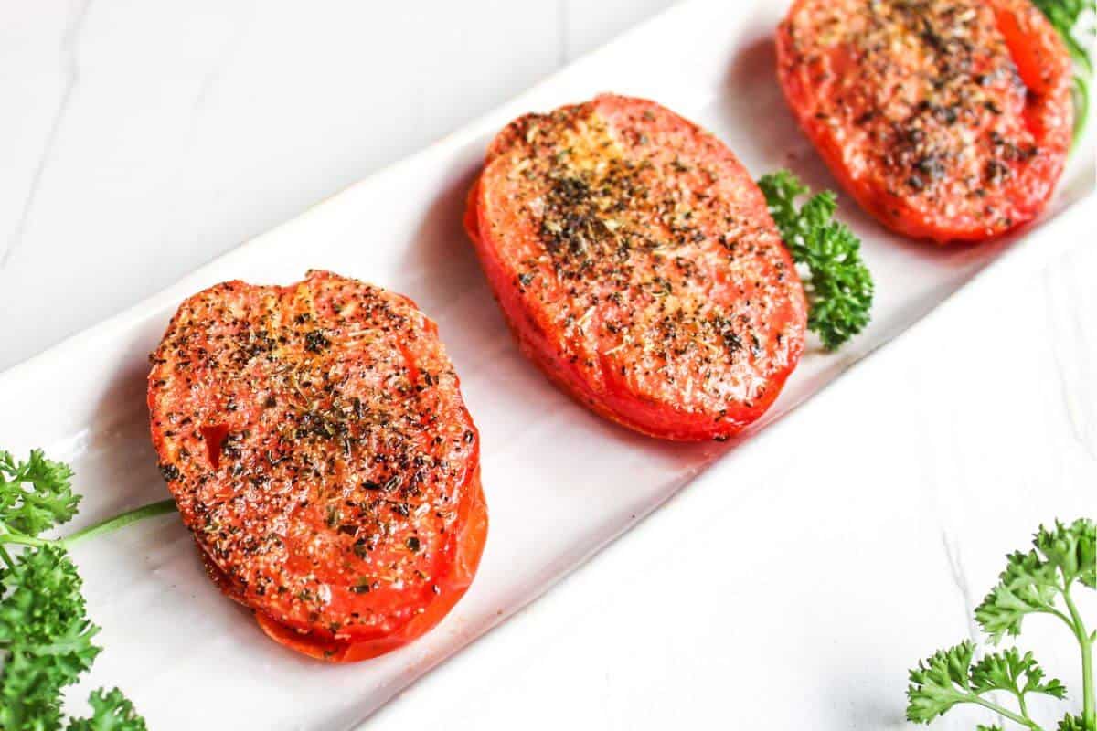 Three air fryer roasted tomatoes on a white plate with parsley.