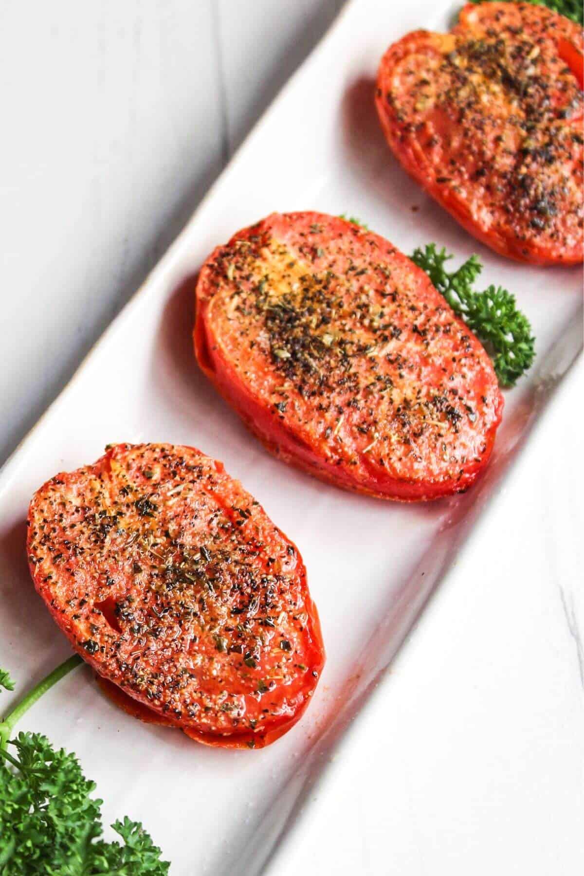 Three air fryer roasted tomatoes on a white plate with parsley.