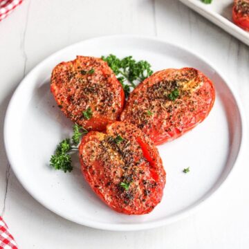 Air fryer roasted tomatoes on a white plate with parsley.
