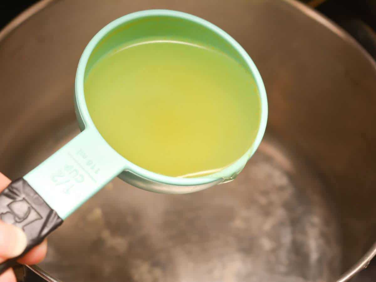A person pouring chicken broth into a pot.