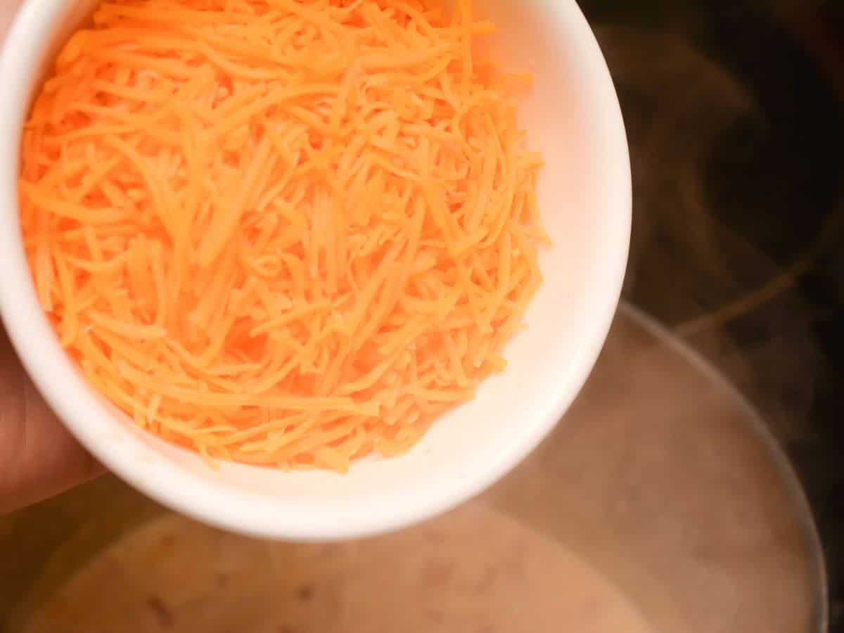 A person dumping grated cheese into a pot.