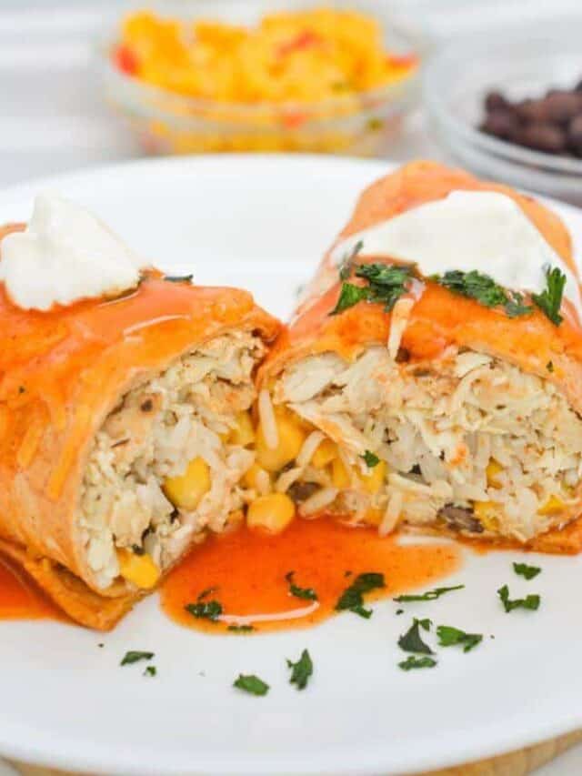 Burrito cut in half, filled with chicken, rice, and corn, topped with spicy sauce and sour cream, served on a white plate with herbs sprinkled around.