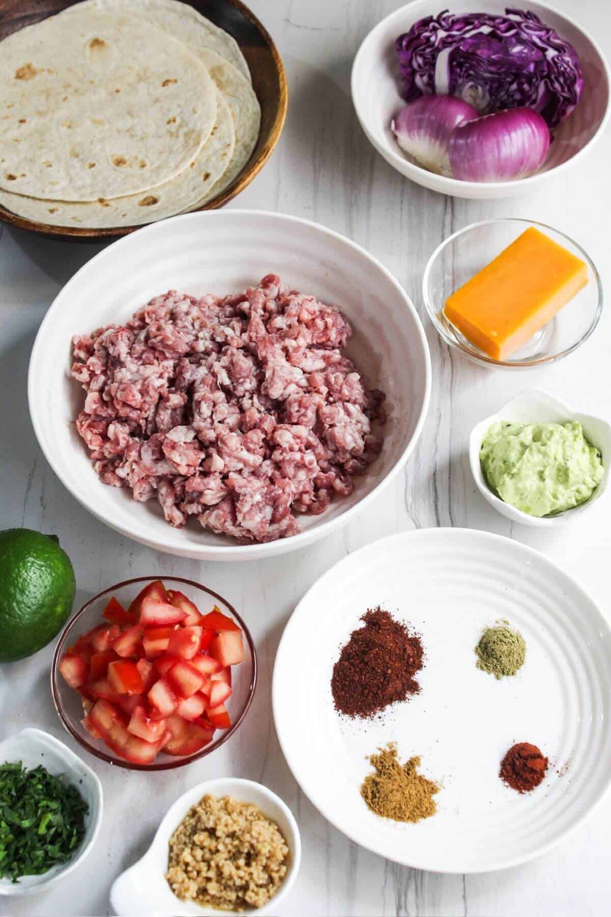 Ingredients for ground pork tacos on a white marble table.