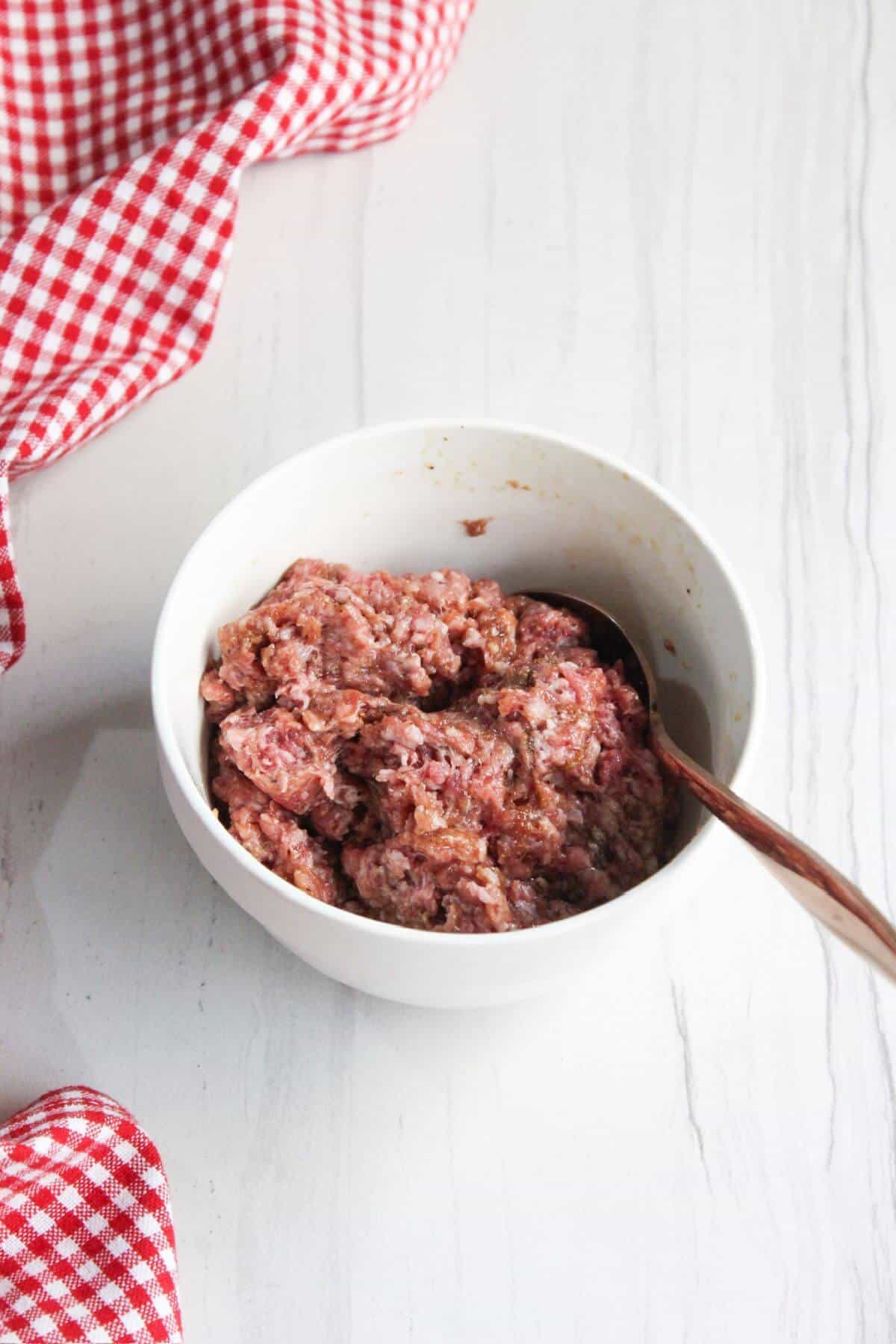 A bowl of seasoned ground pork in a red and white checkered tablecloth.