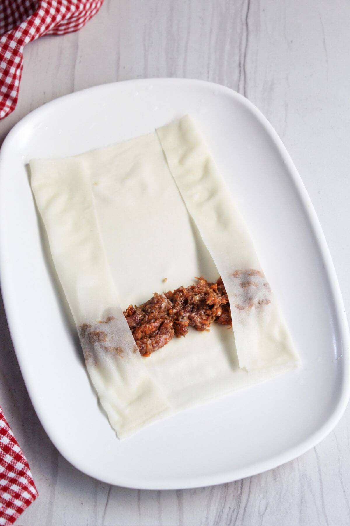 Folding lumpia wrapper over meat mixture.