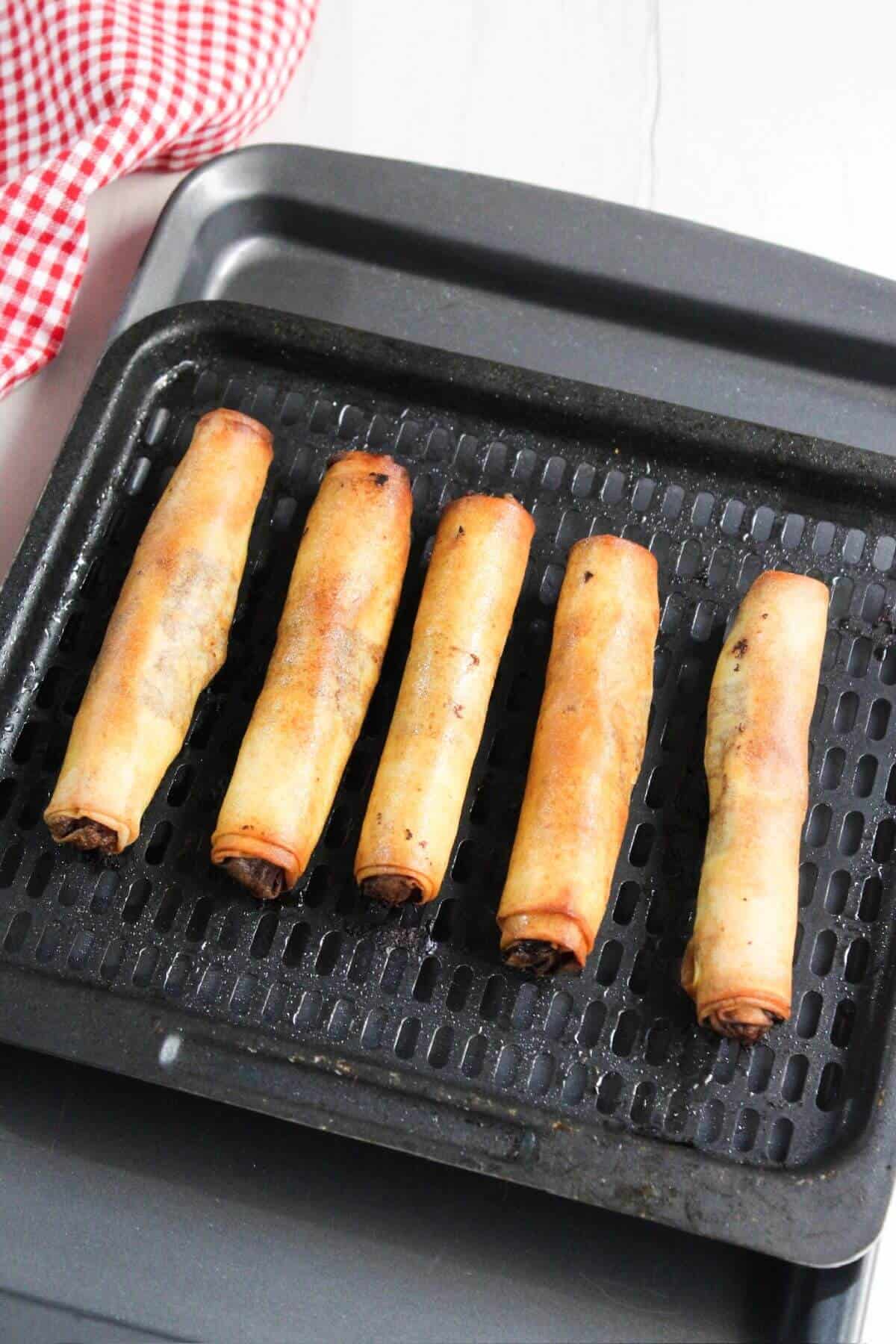Air fried lumpia on air fryer pan with a red checkered cloth.