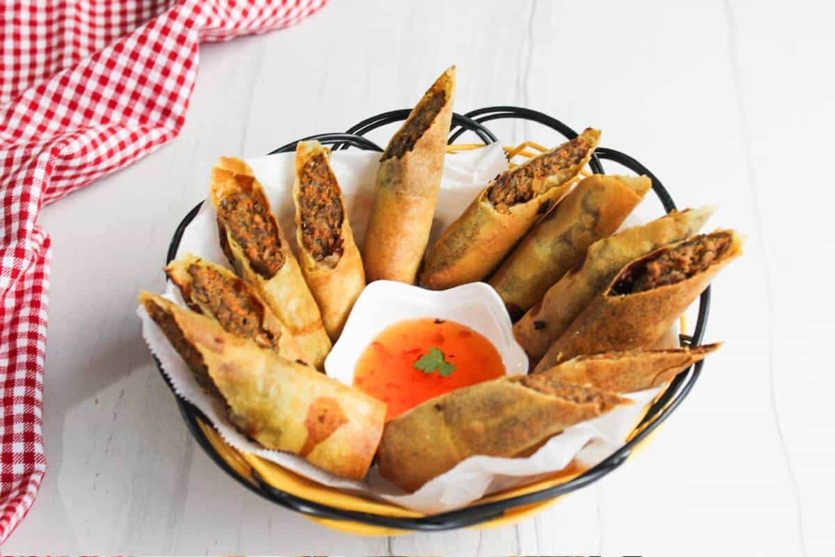 Filipino lumpia in a basket with dipping sauce.