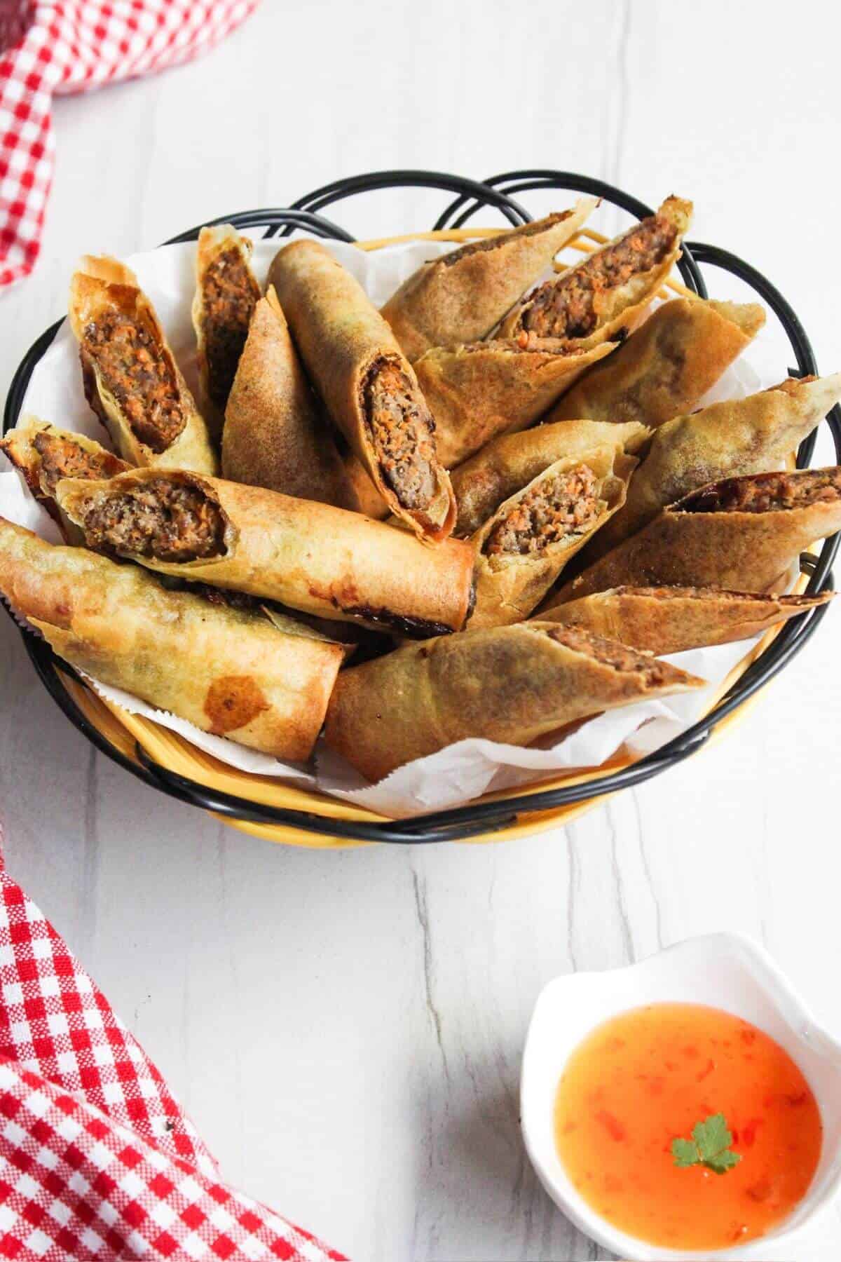 Filipino lumpia in a bowl with dipping sauce.