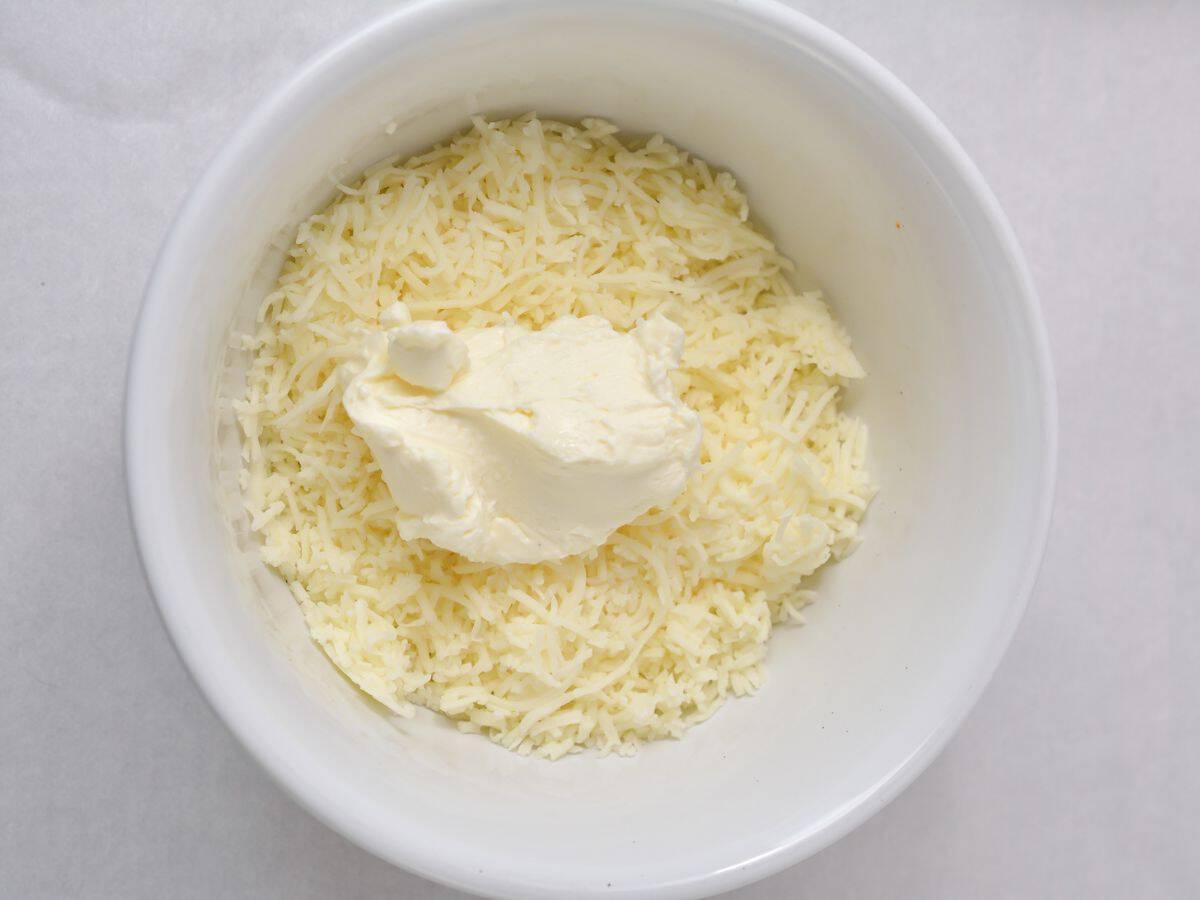 A bowl filled with shredded mozzarella cheese and cream cheese.