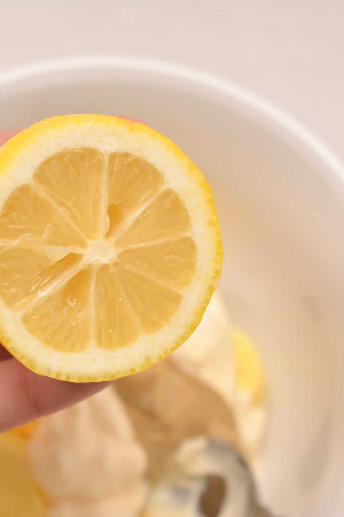 A person holding a slice of lemon over a bowl.