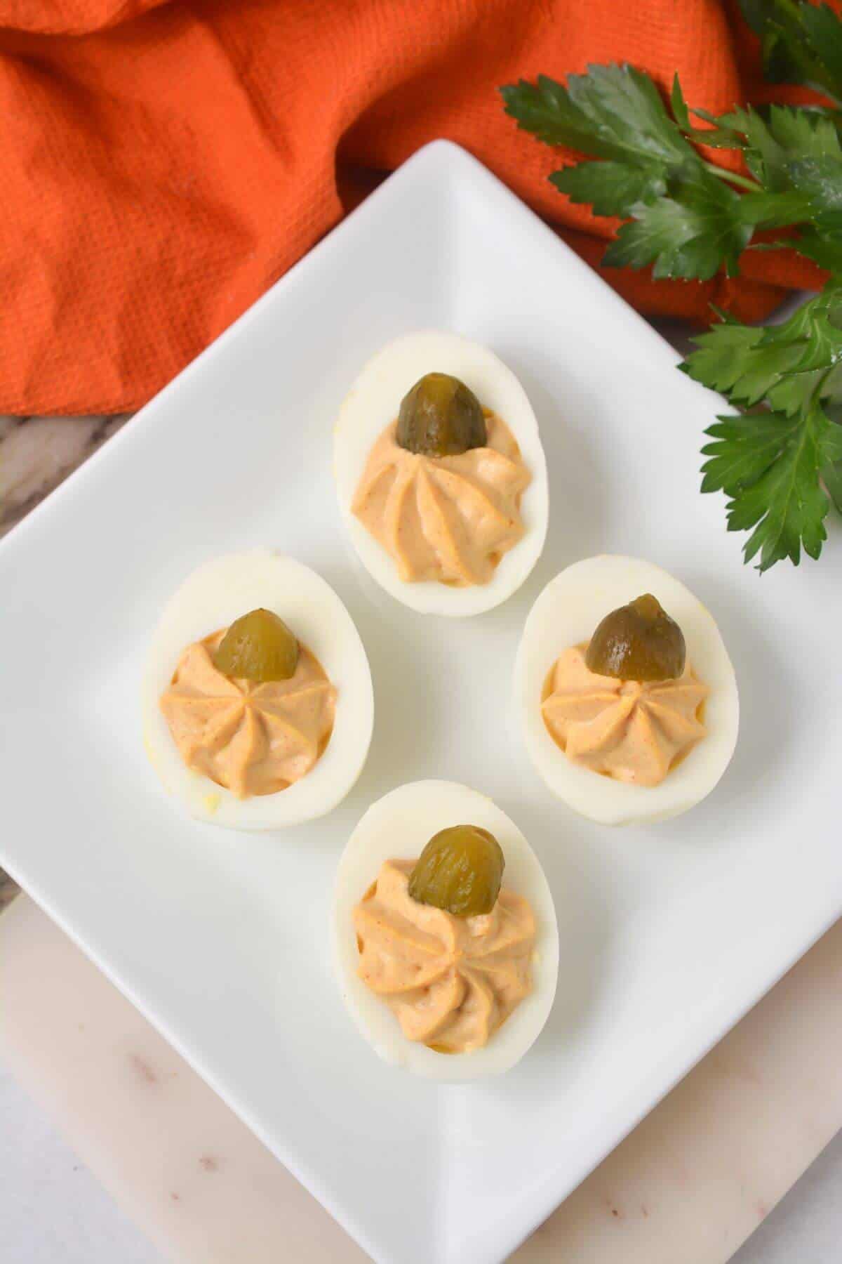 Deviled eggs for Halloween on a white plate with pumpkin.