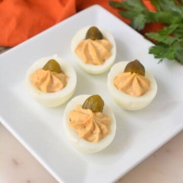 Pumpkin deviled eggs on a white plate with parsley.