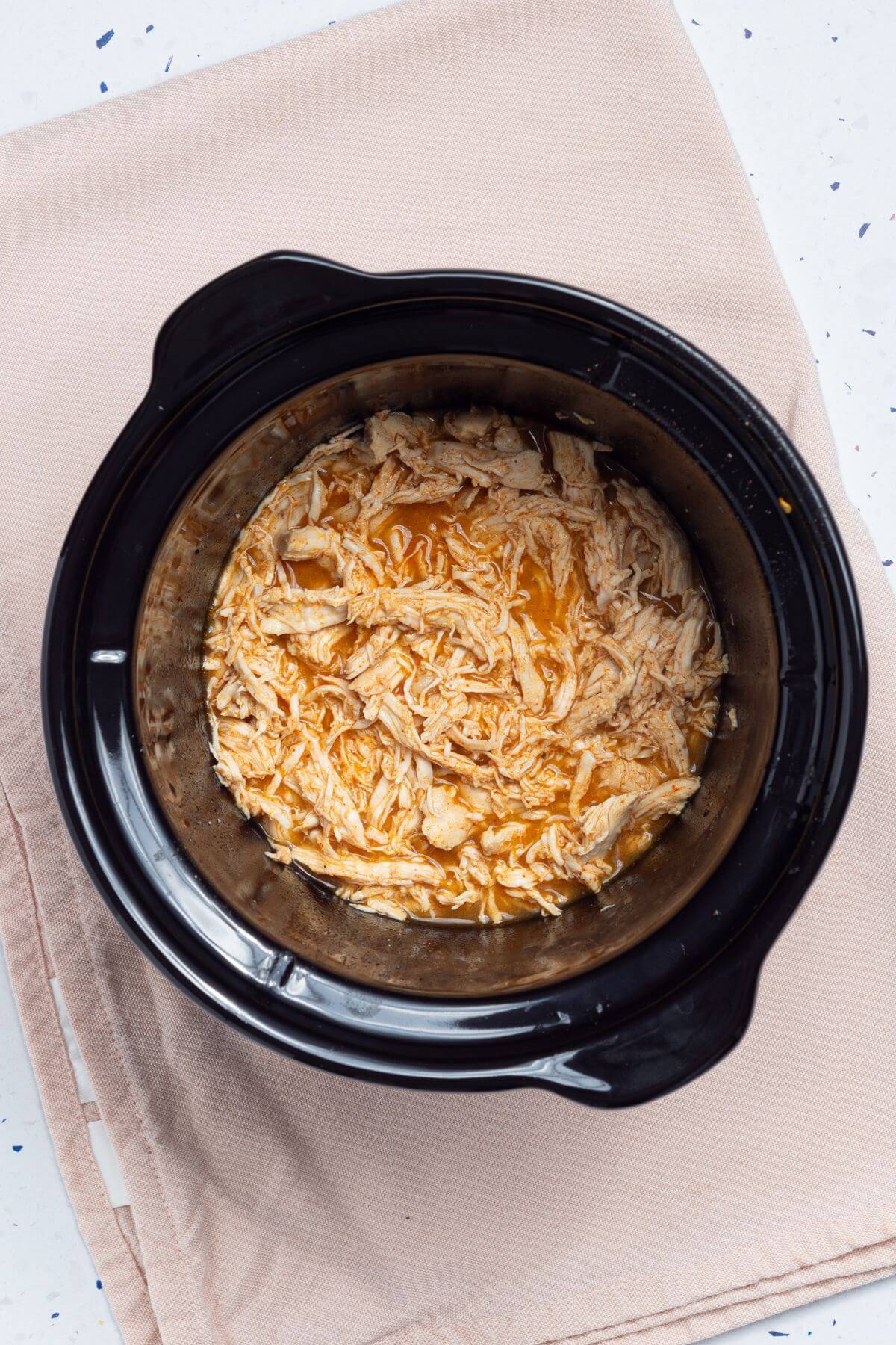 A crock pot with shredded chicken for tacos in it.