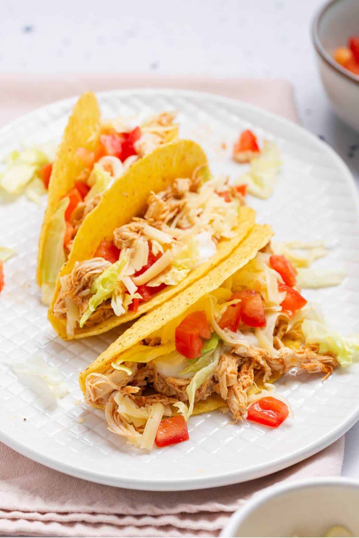 Three tacos on a plate with tomatoes and lettuce.