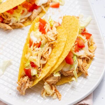 Three chicken tacos on a white plate.