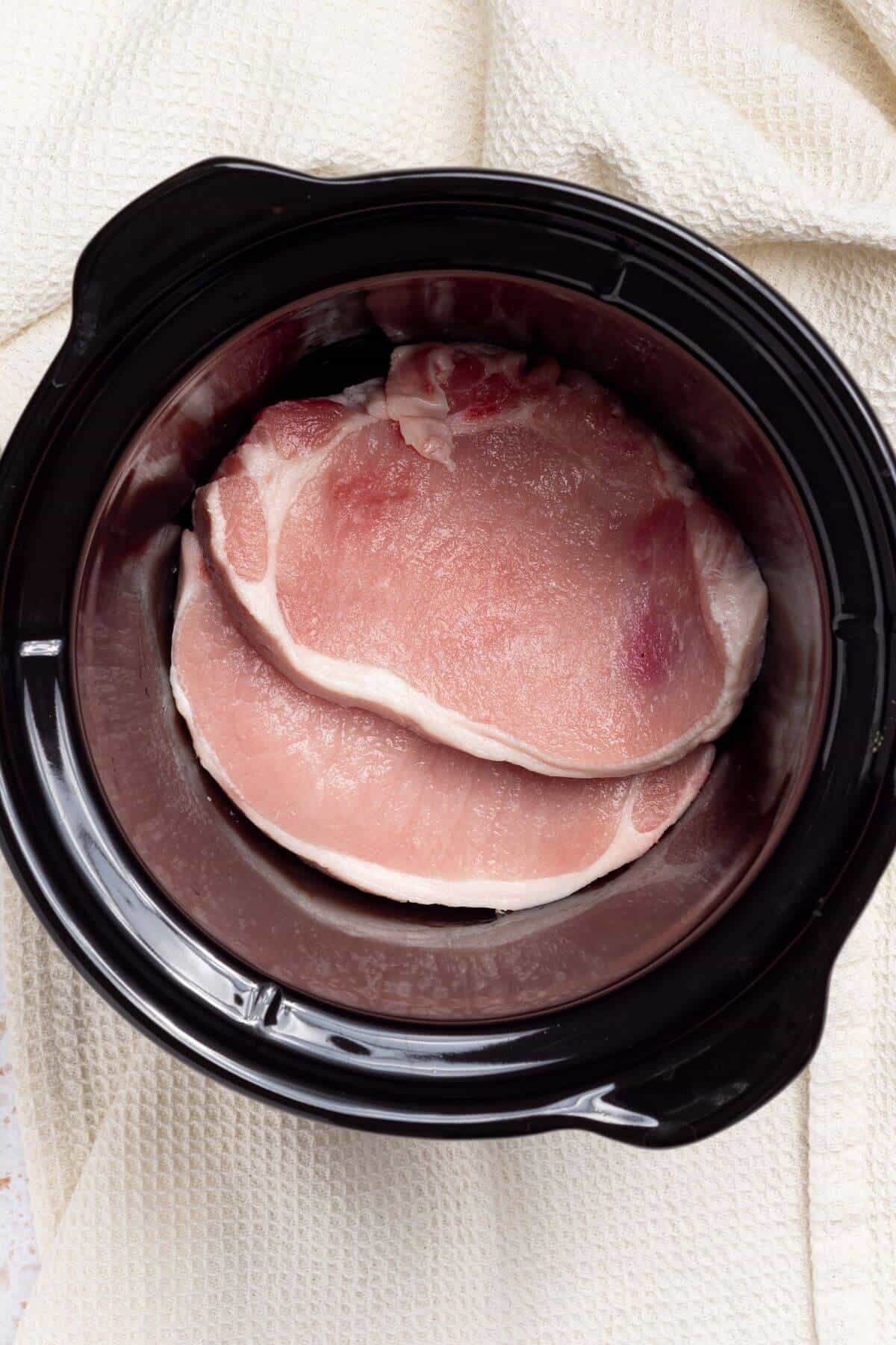 Pork chops in a slow cooker on a white background.