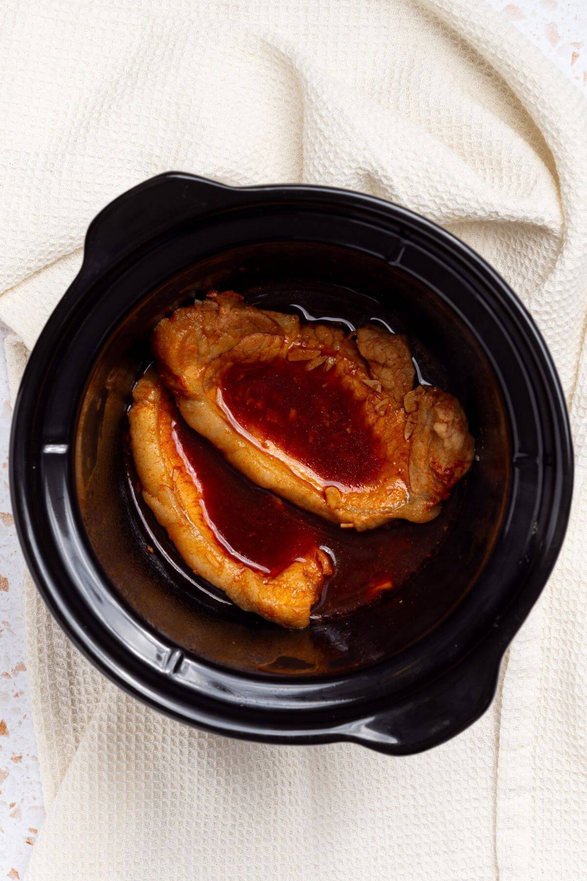 Pork chops in a slow cooker with sauce on a white background.