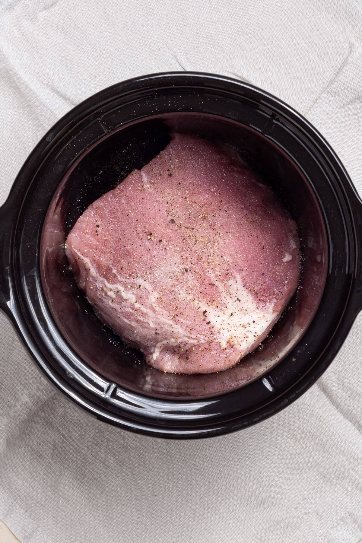 A piece of seasoned pork loin in a black crock pot.
