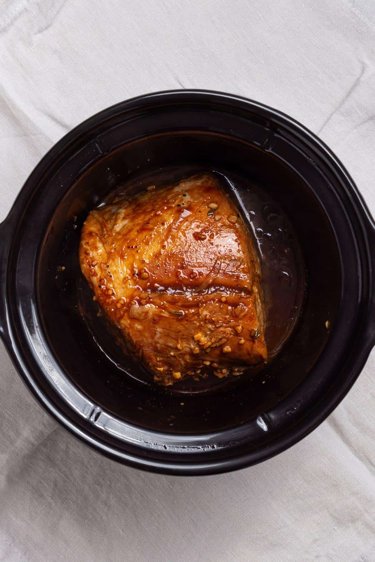 A crock pot with a piece of cooked pork loin in it.