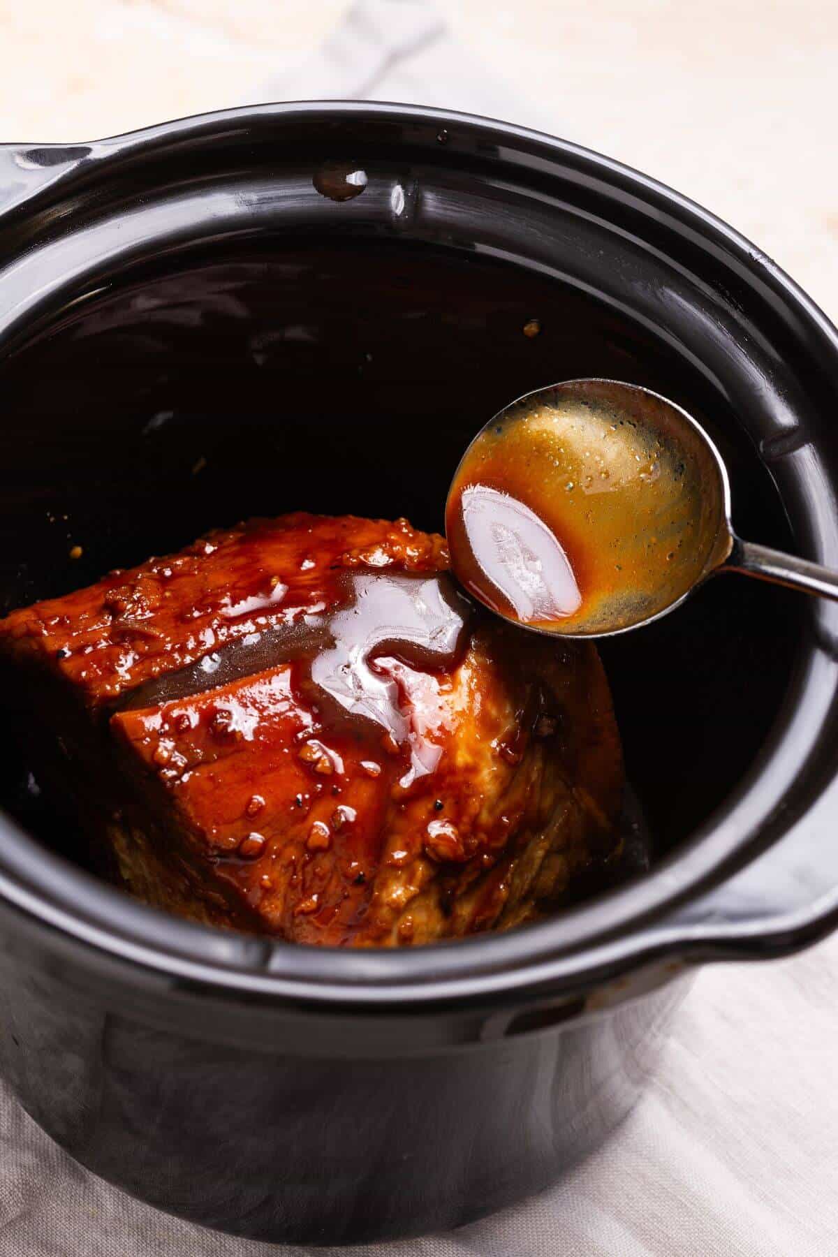 Pouring sauce over cooked pork loin in crock pot.