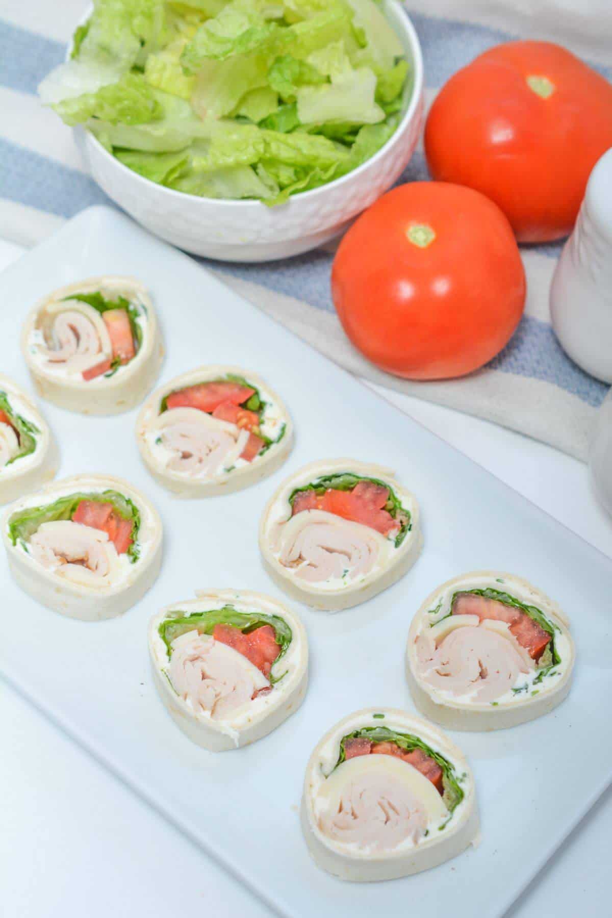 A white plate with a tray of chicken and tomato wraps.