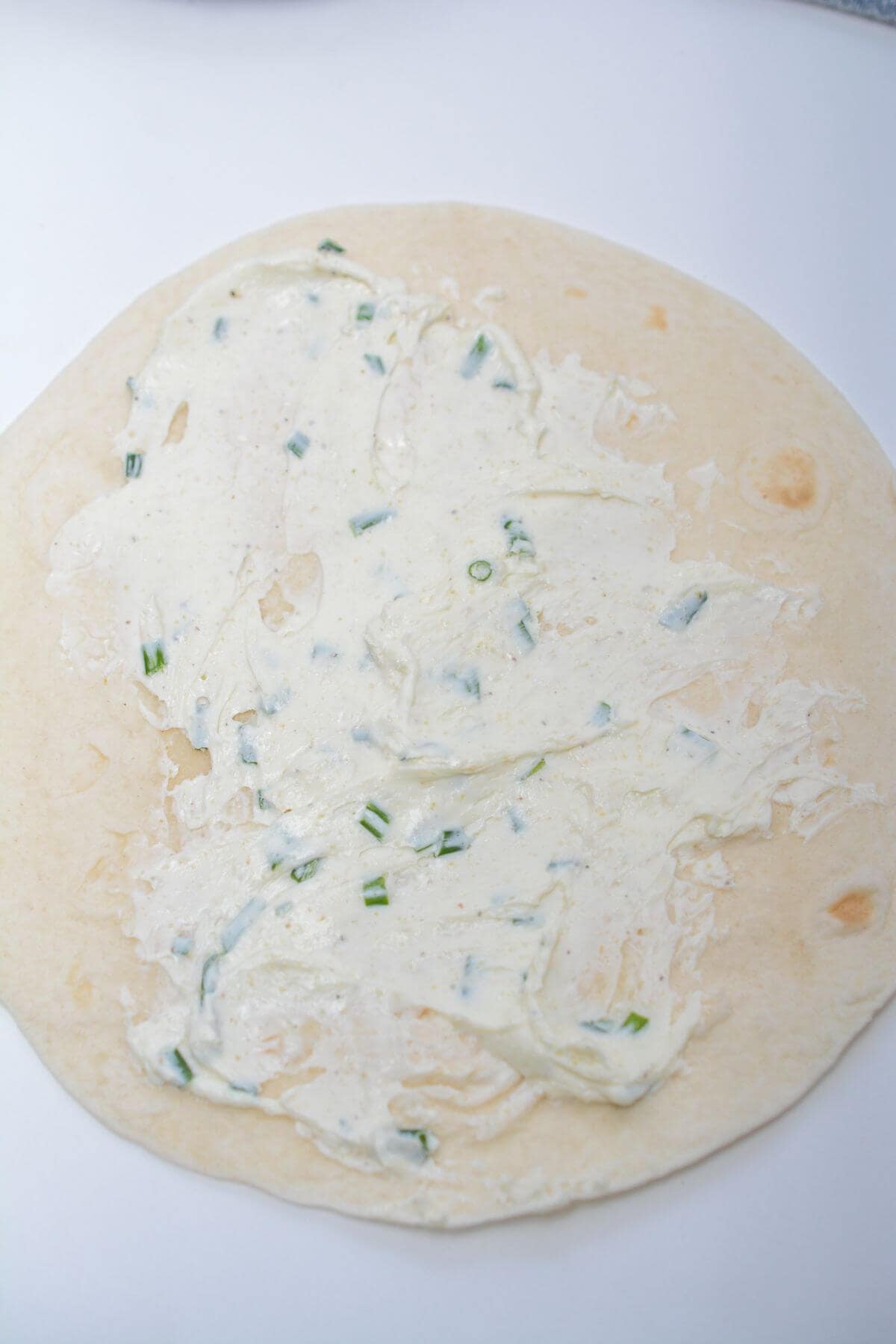 A tortilla with cheese and green onions on it.
