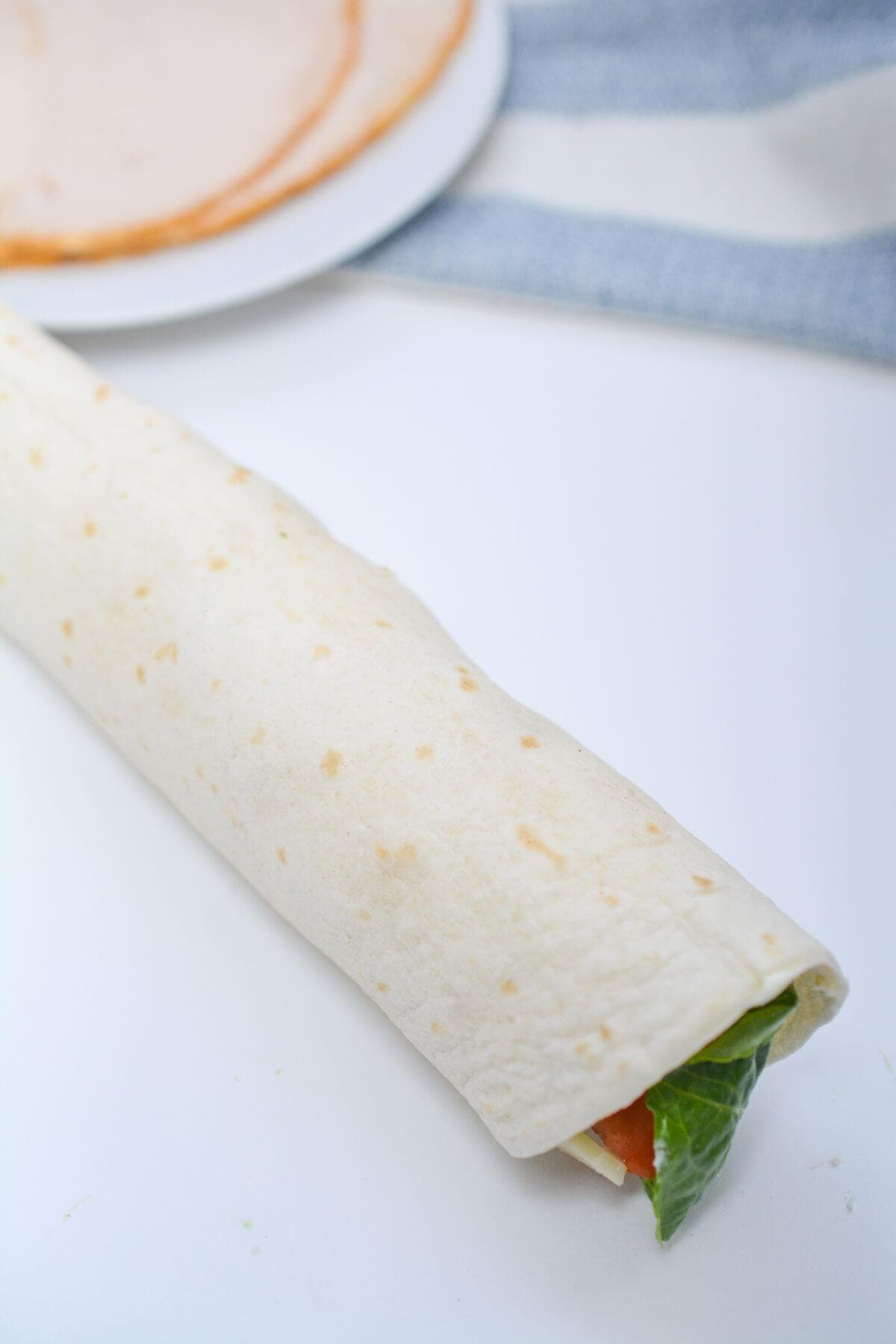 A tortilla wrap is sitting on a table next to a plate.