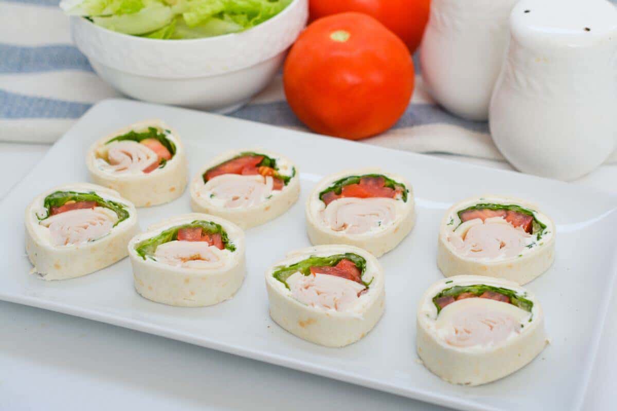 A plate of turkey roll-up pinwheels with tomatoes and lettuce.