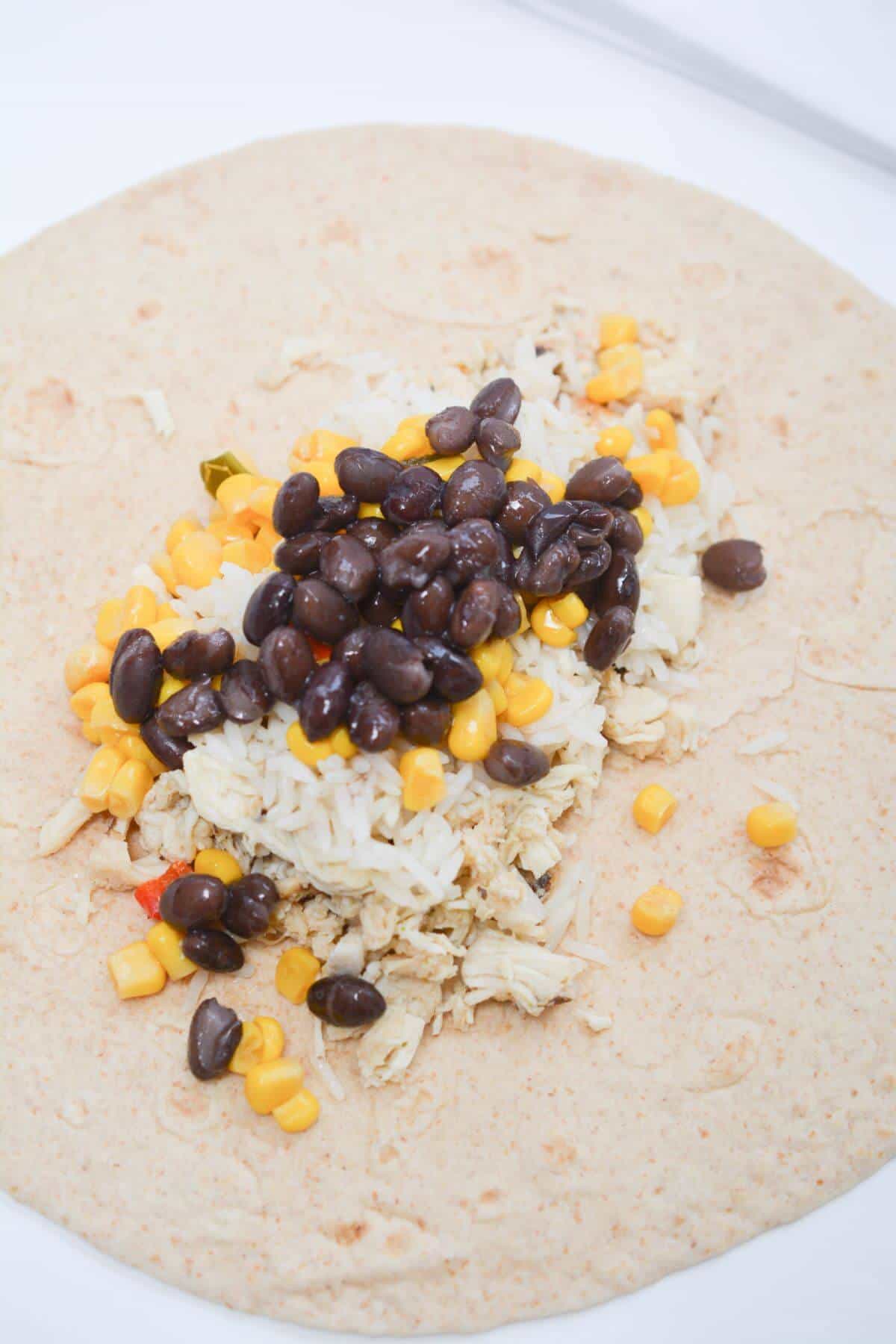 A tortilla with black beans and corn on it.