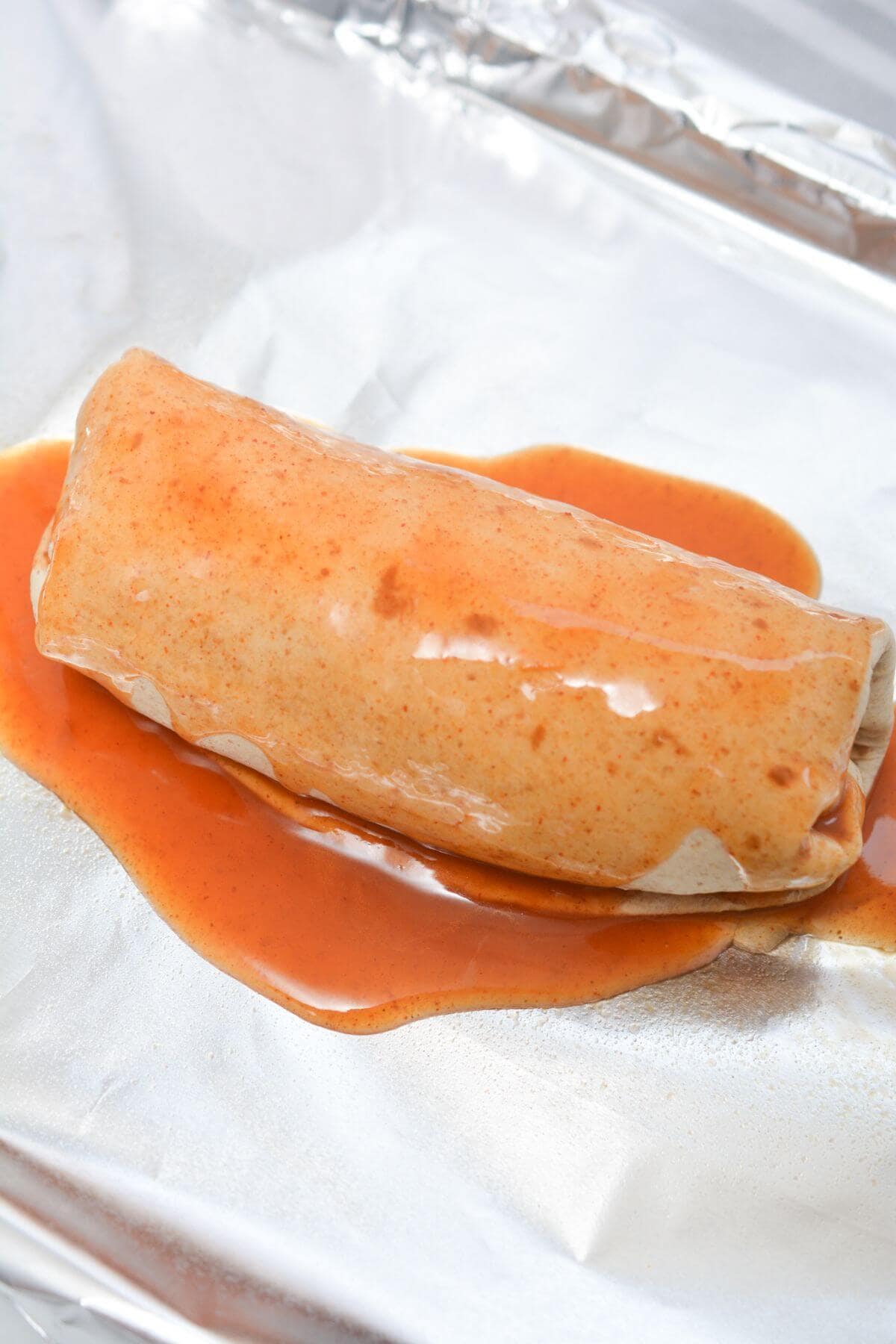 A burrito with sauce on a piece of foil.