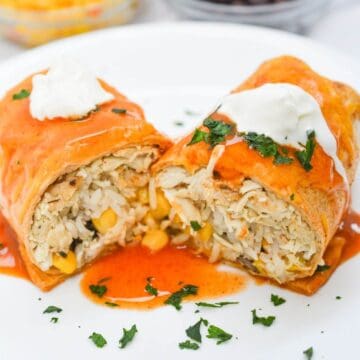 Wet burrito with sauce and sour cream on a plate.
