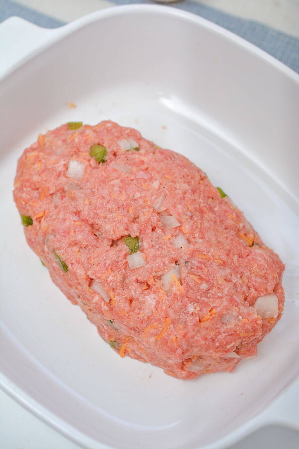 Uncooked meatloaf in a white dish.