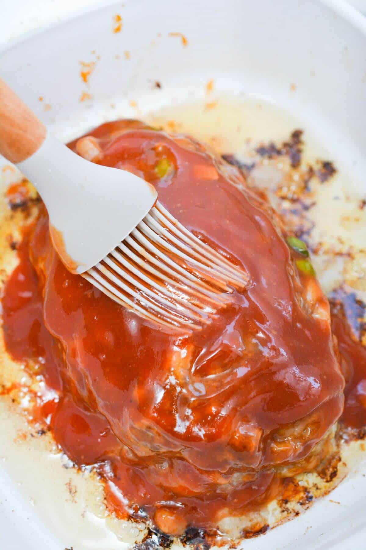 A brush is being used to brush sauce onto meatloaf.