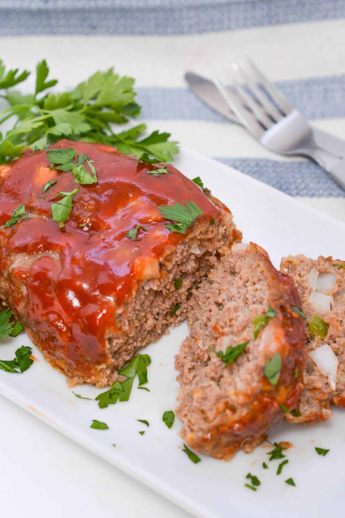 Meatloaf on a white platter with sauce and parsley.