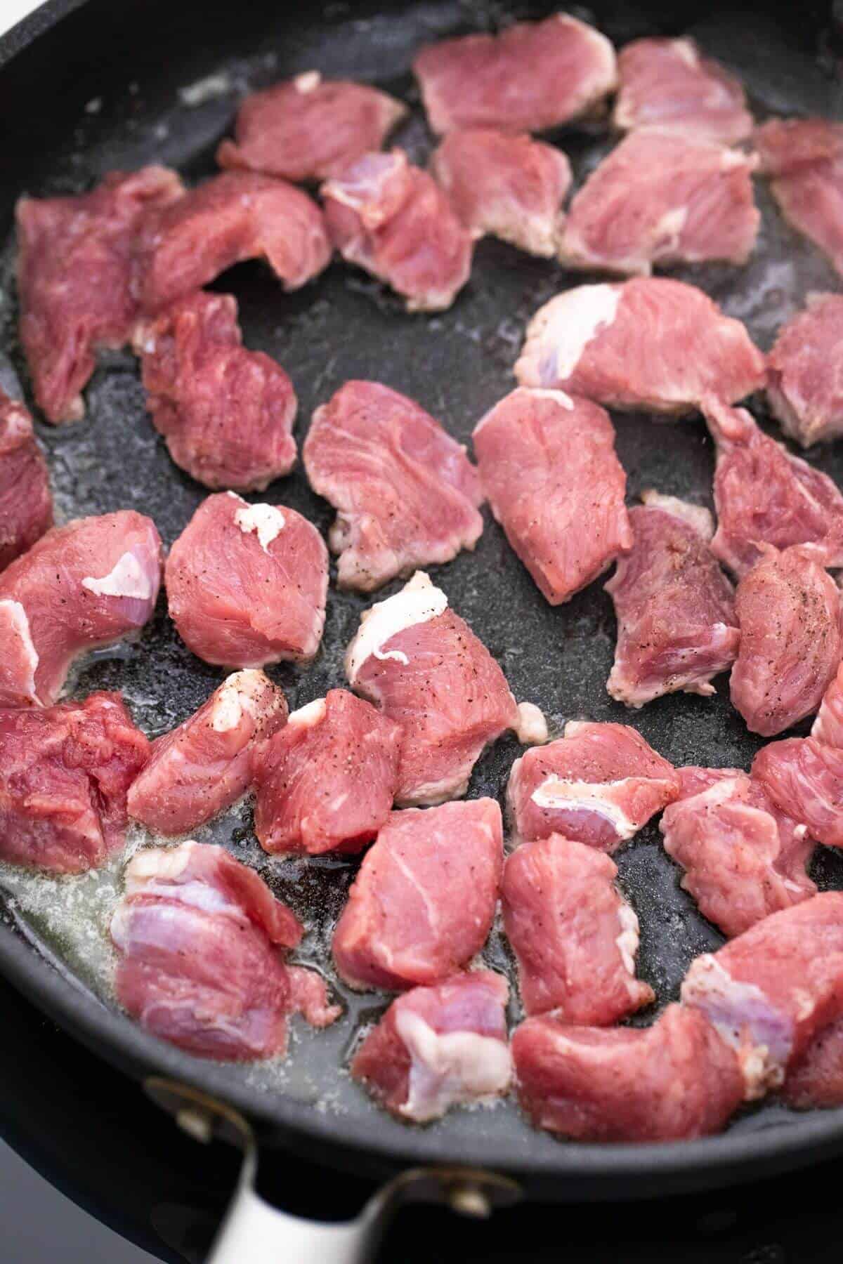 A frying pan with cubed beef in it.