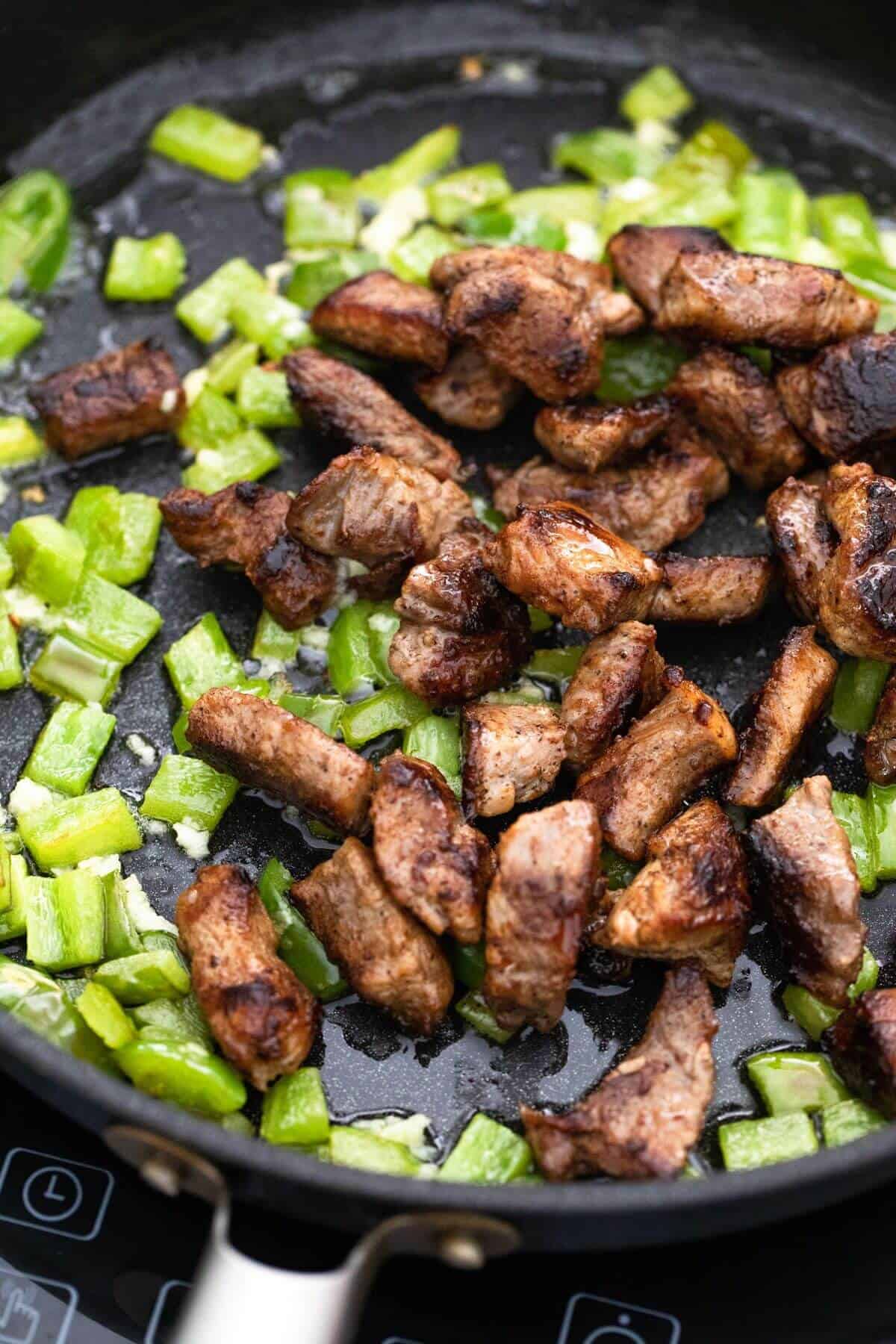 A frying pan with meat and green pepper.