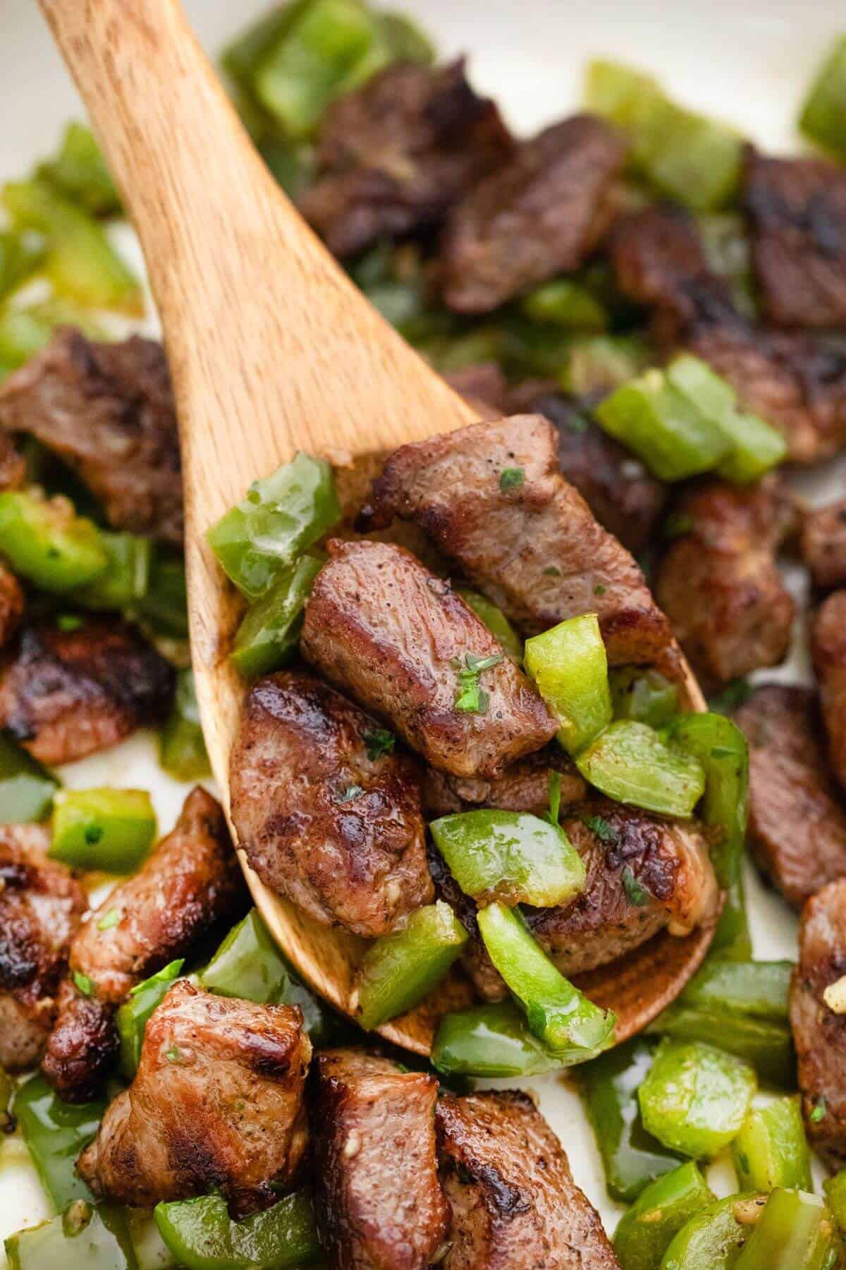 A wooden spoon filled with meat and green pepper.